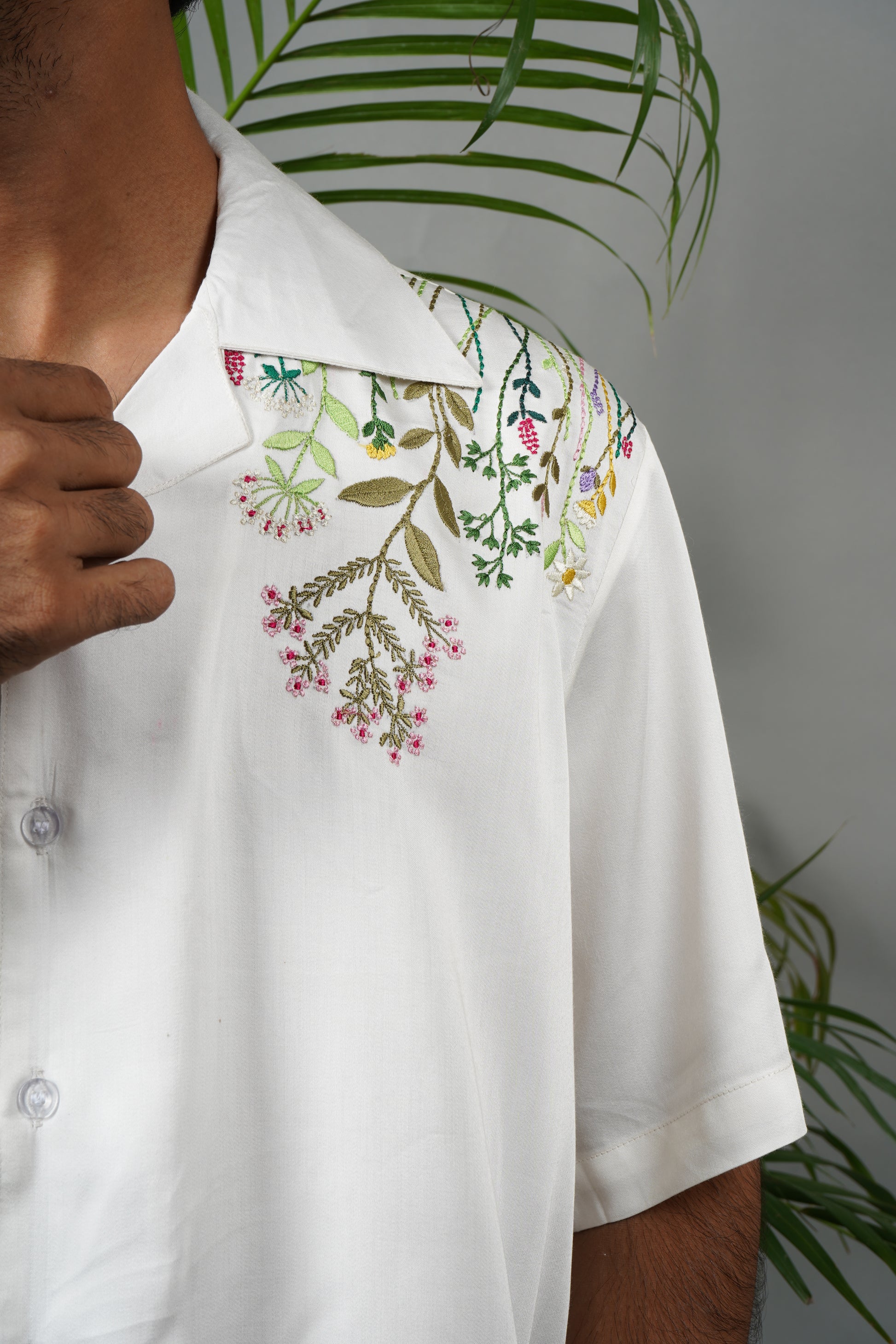 "Handmade white Cuban collar shirt made from soft modal fabric with intricate  embroidery featuring floral and leaf patterns on the shoulder and pocket."

