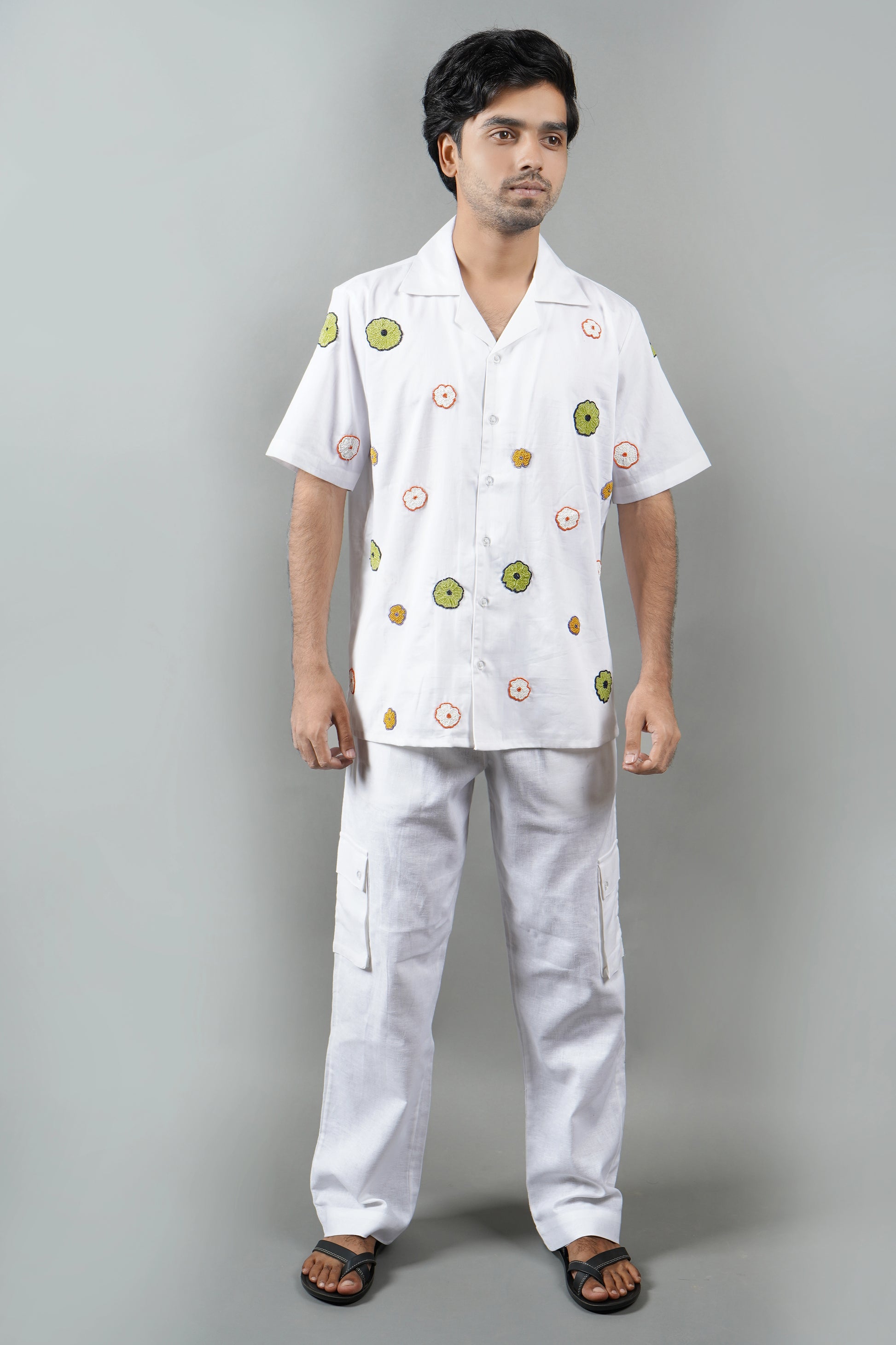 "White Cuban collar shirt with vibrant hand-embroidered floral motifs in green, orange, and yellow. Perfect for a relaxed, luxury look. Made from breathable cotton fabric."
