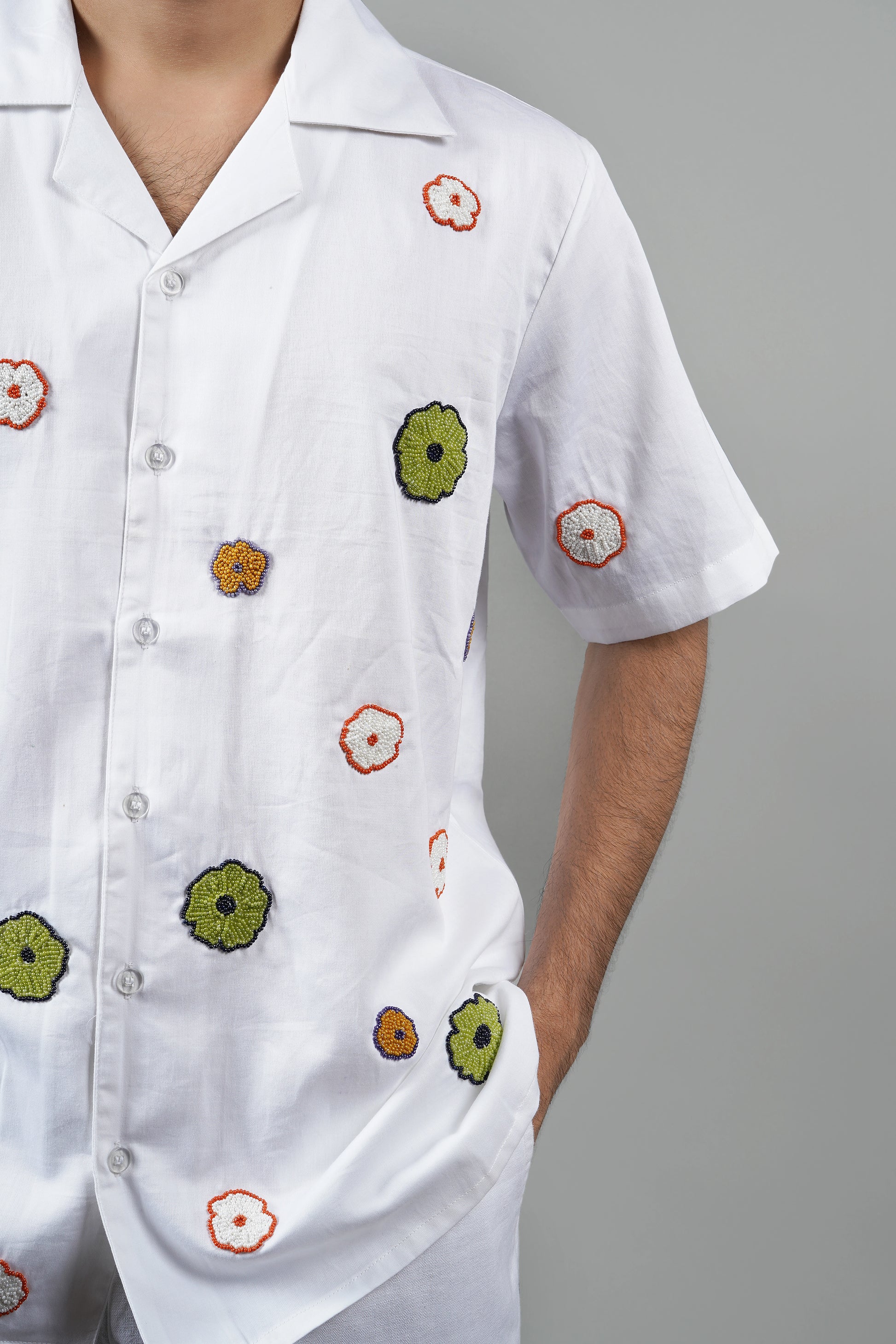 "White Cuban collar shirt with vibrant hand-embroidered floral motifs in green, orange, and yellow. Perfect for a relaxed, luxury look. Made from breathable cotton fabric."
