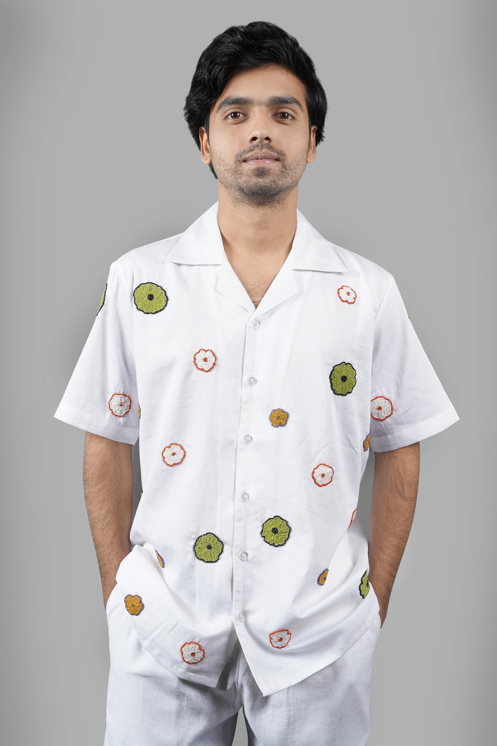 "White Cuban collar shirt with vibrant hand-embroidered floral motifs in green, orange, and yellow. Perfect for a relaxed, luxury look. Made from breathable cotton fabric."
