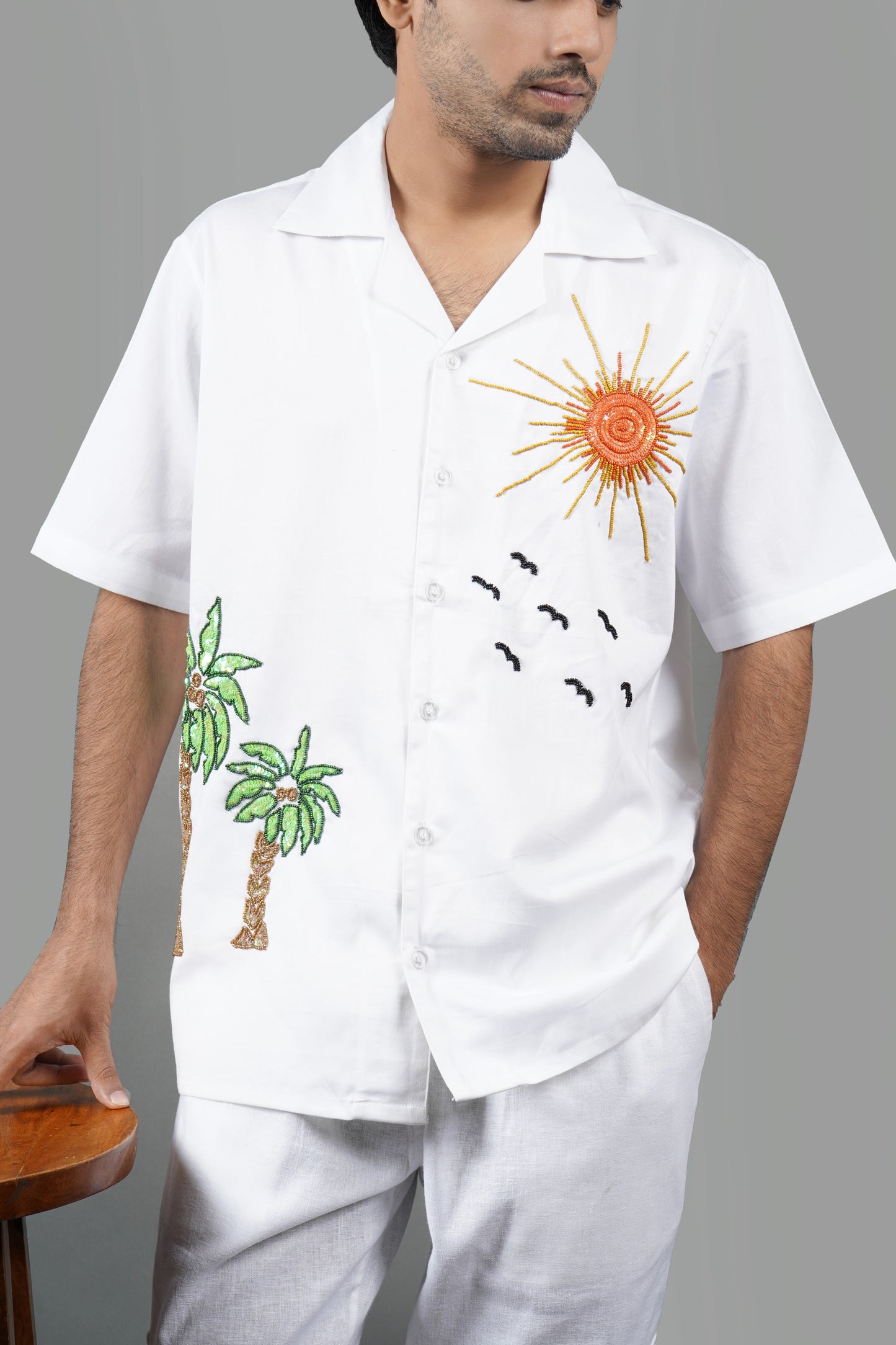 Handmade white cotton shirt with vibrant hand-embroidered tropical palm tree and sun design, luxury summer wear for men, unique artisanal embroidery.

