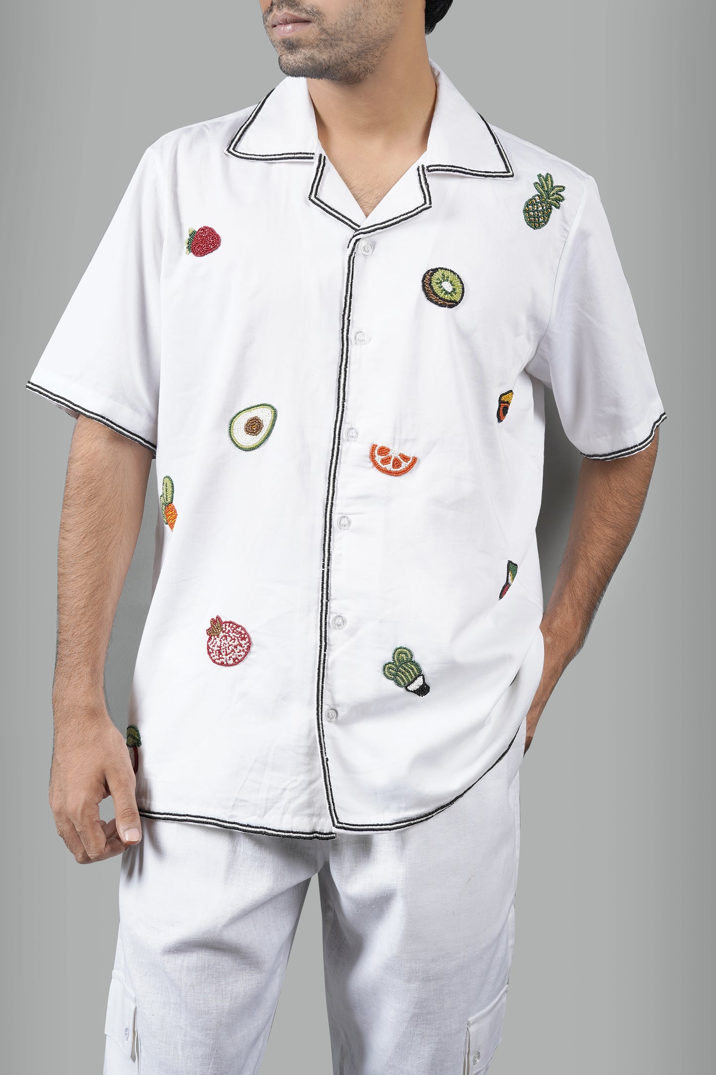 "White Cuban collar shirt featuring colorful hand-embroidered fruits like avocado, orange, kiwi, and pomegranate. Stylish and lightweight for a casual yet unique statement look."

