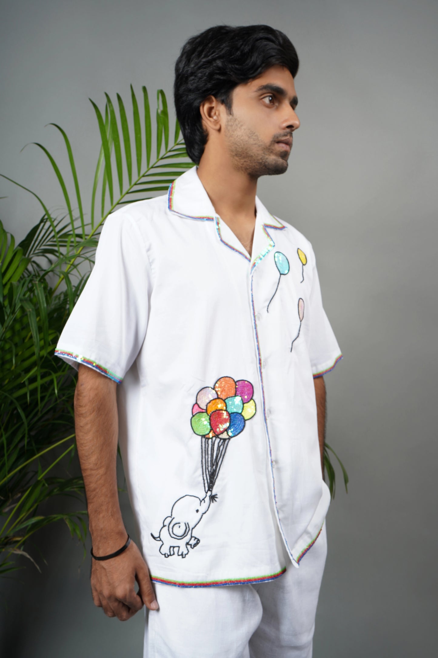 "White Cuban collar shirt with playful hand embroidery of colorful balloons and rainbow piping details. Modern and artistic design made from breathable, premium cotton fabric."

