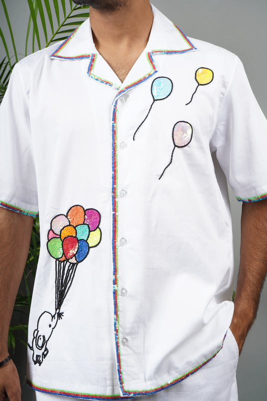 "White Cuban collar shirt with playful hand embroidery of colorful balloons and rainbow piping details. Modern and artistic design made from breathable, premium cotton fabric."
