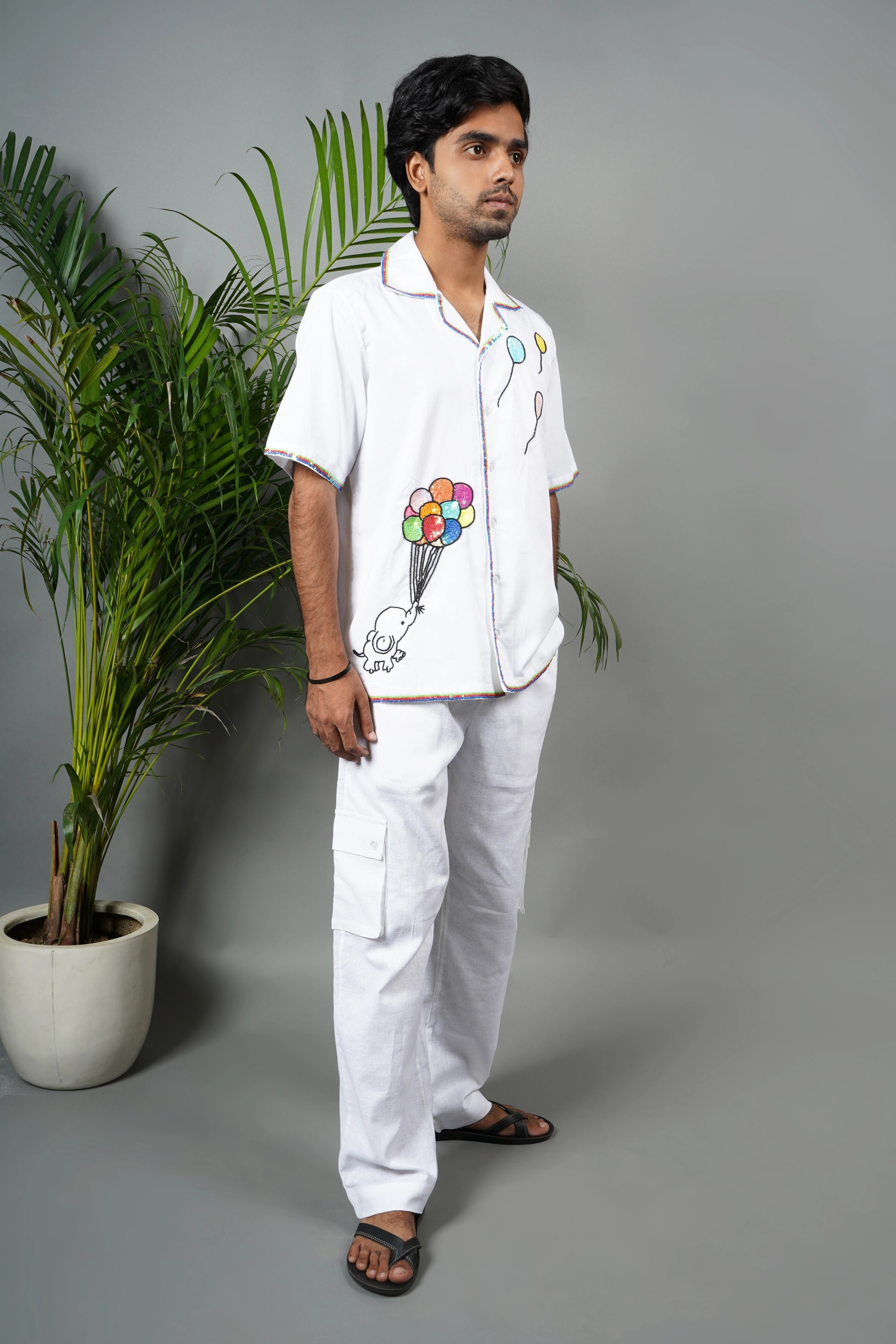 "White Cuban collar shirt with playful hand embroidery of colorful balloons and rainbow piping details. Modern and artistic design made from breathable, premium cotton fabric."

