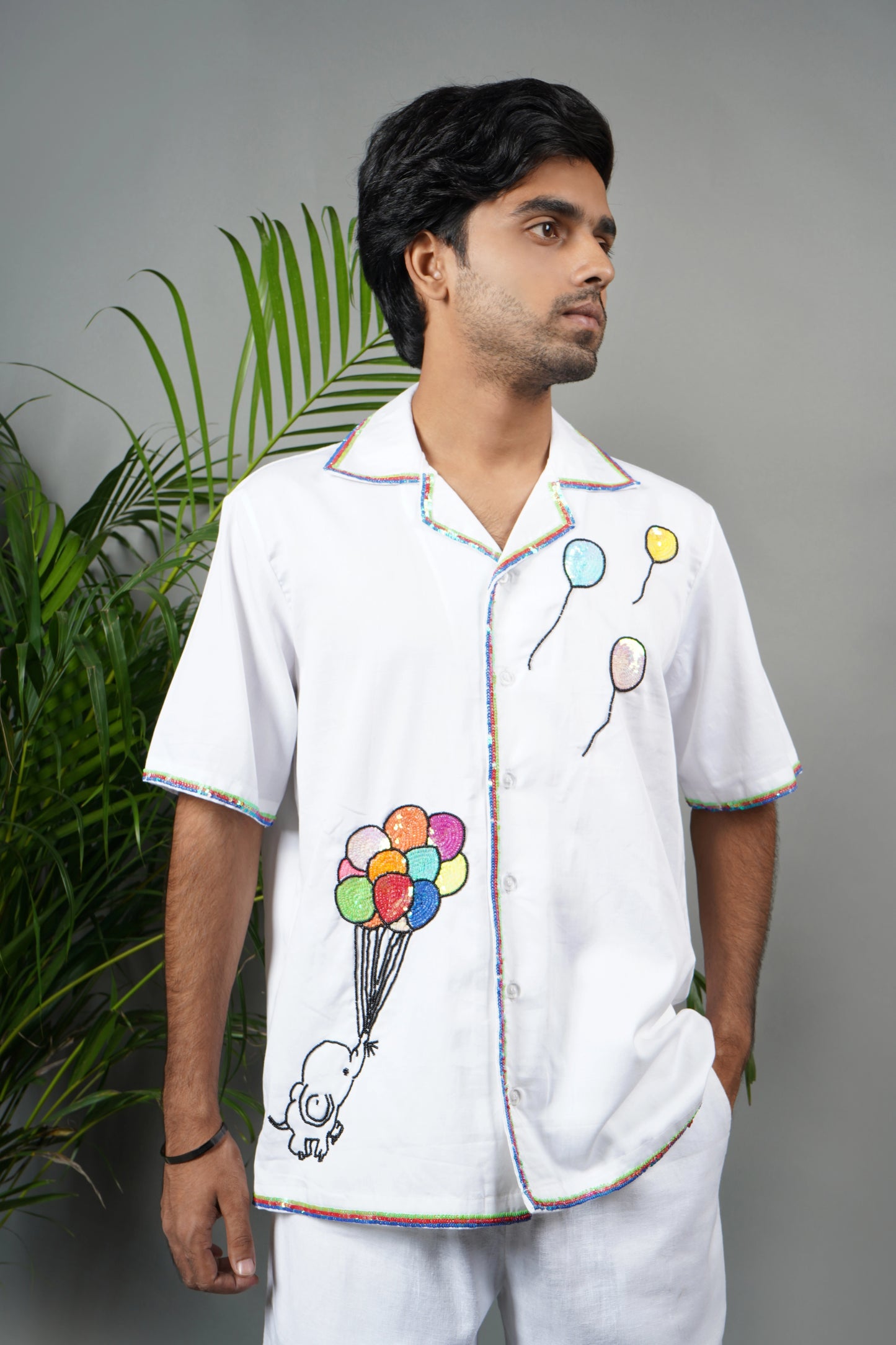 "White Cuban collar shirt with playful hand embroidery of colorful balloons and rainbow piping details. Modern and artistic design made from breathable, premium cotton fabric."

