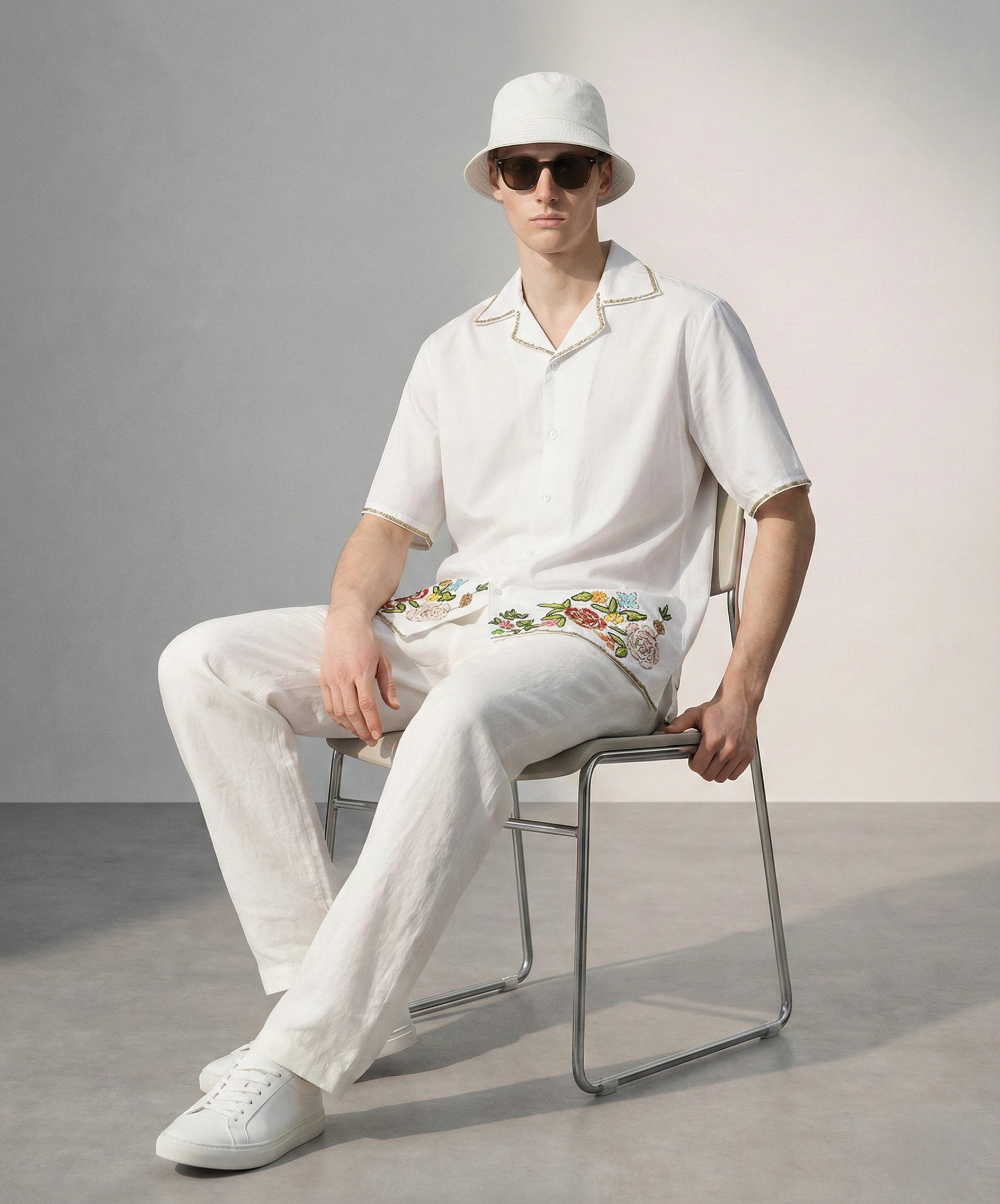 Man sitting wearing white embroidered Cuban collar cotton shirt with floral design, luxury handmade summer outfit