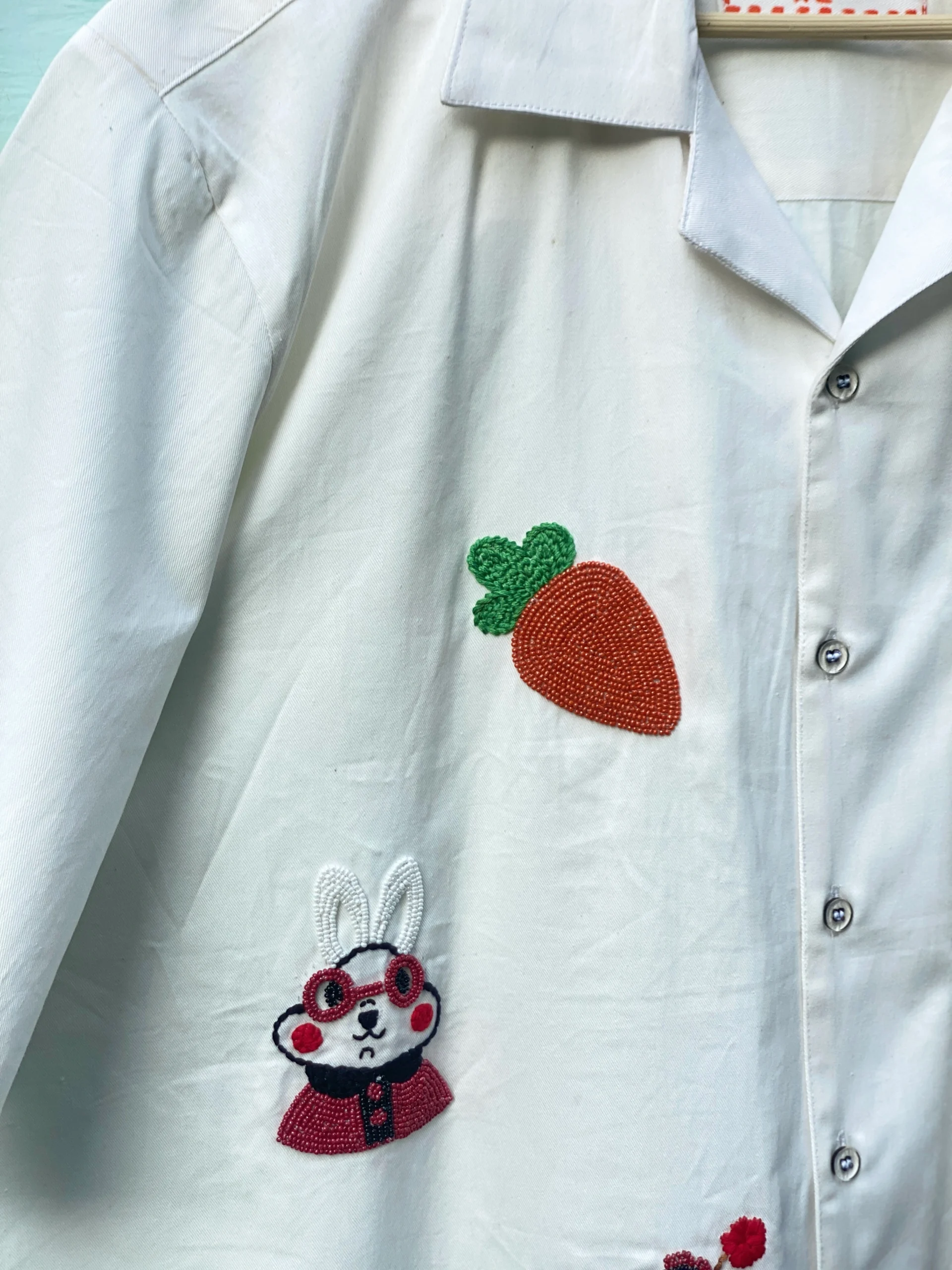 "Handmade cotton shirt with colorful hand embroidery, moti work, and fabric paint featuring motifs like bunny, umbrella girl, cherries, chicken, and carrot – limited edition Cuban collar shirt by Liibula"