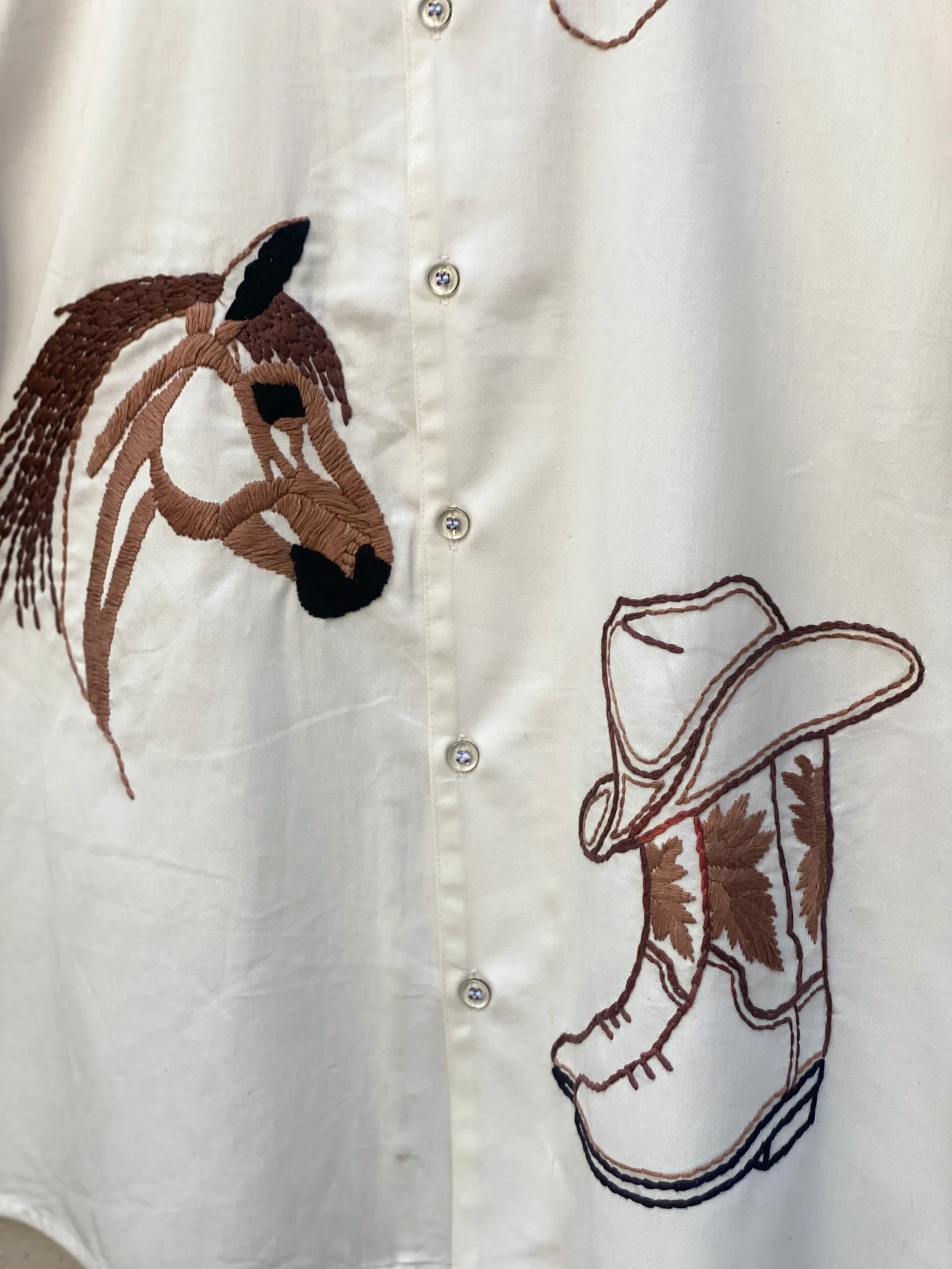 Macro close up of handmade cowboy embroidery with horse and boots design on mens shirt, high quality artisan stitching on linen fabric
