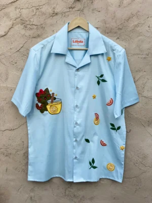 Le Citrus Cat Cuban collar shirt displayed on hanger against wall background.