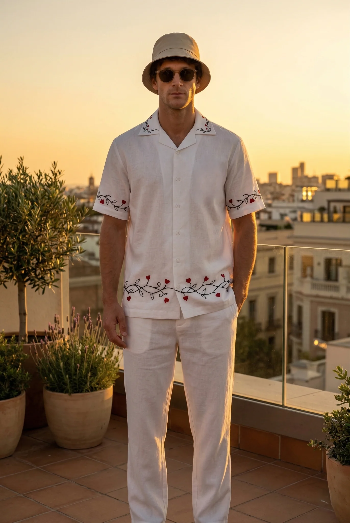 Men white linen shirt with red heart embroidery standing on rooftop at sunset, luxury summer outfit, breathable cotton linen clothing