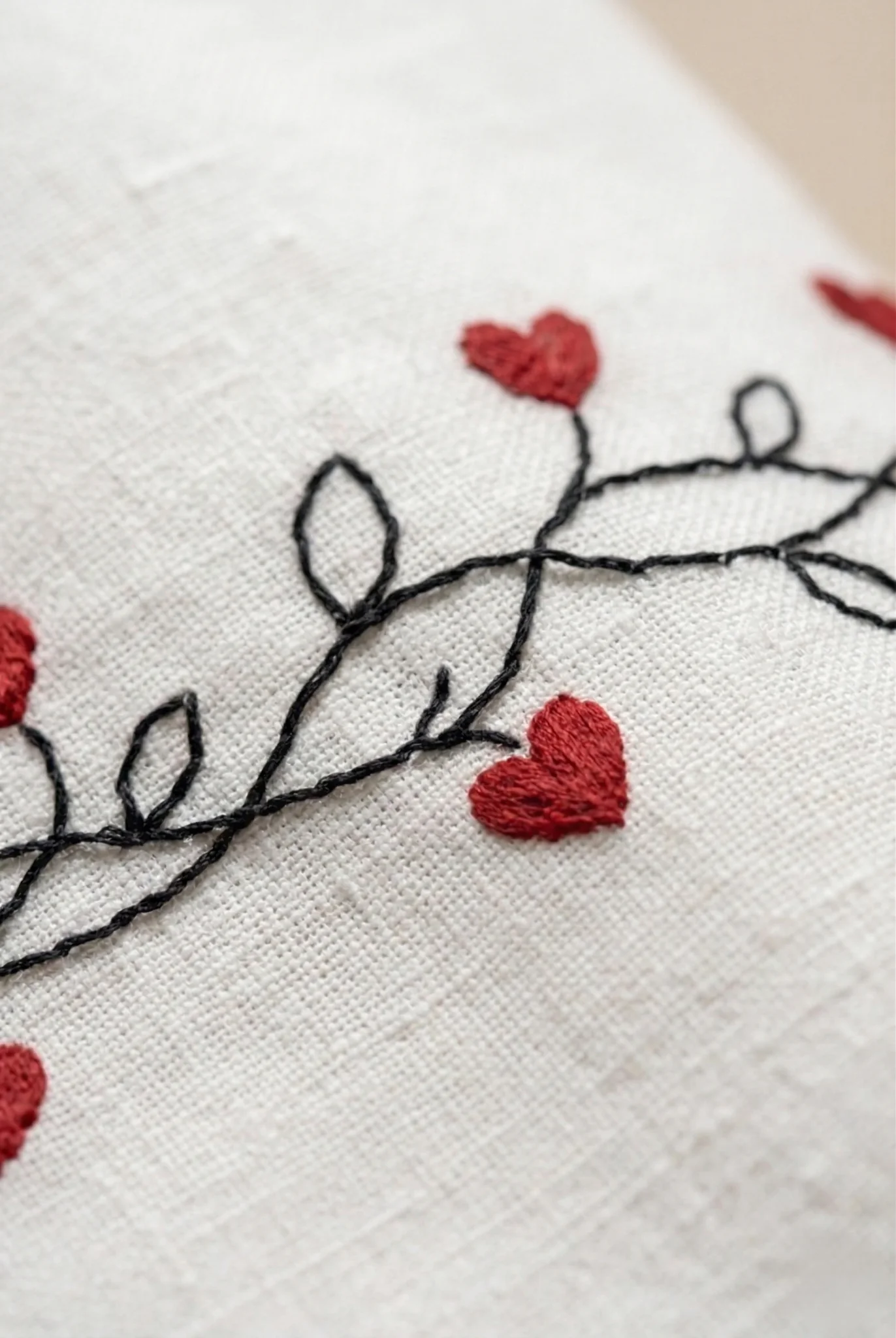 Close-up of hand embroidered red heart vine design on white linen fabric, detailed artisan embroidery, premium handmade shirt texture