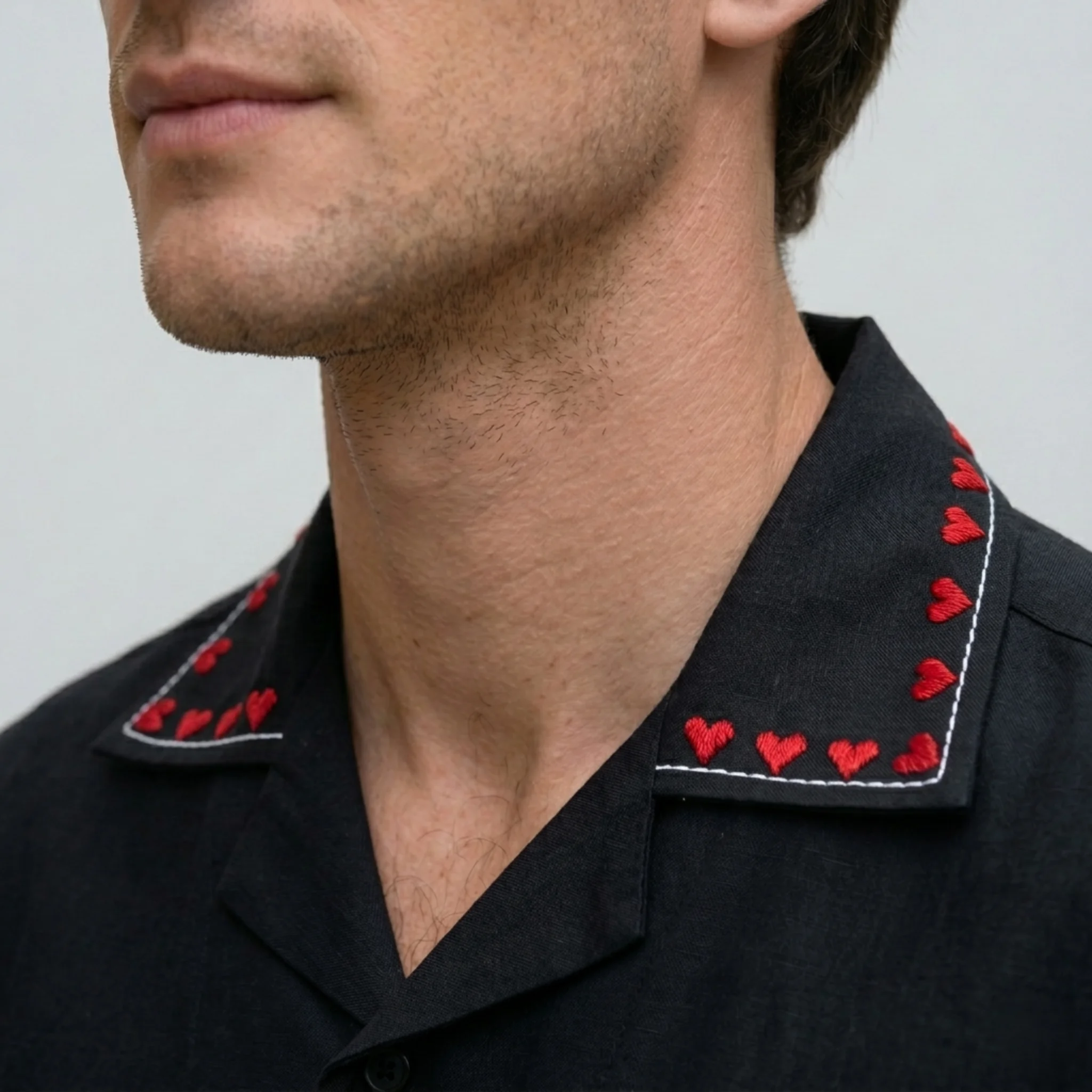 Hand embroidered red heart detail on black Cuban collar shirt, premium cotton fabric close-up, luxury handmade mens shirt embroidery detail